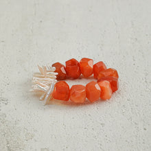 Faceted orange carnelian bead ring with irregular white pearl cluster on textured surface