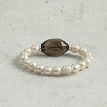 Elegant bracelet featuring white pearls and a central faceted smoky quartz bead on a light textured background