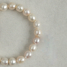 Close-up of a pearl necklace with lustrous white and light pink pearls on a textured gray background