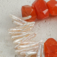 Close-up of white elongated pearls and rough red coral beads on a textured light surface