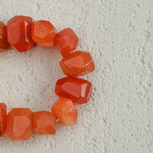 Close-up of faceted orange carnelian gemstone beads on textured light surface