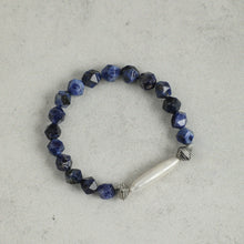 Faceted blue sodalite bead bracelet with silver accents and elongated white pearl on gray background