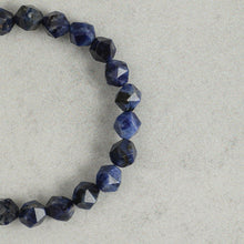 Close-up of a faceted blue sodalite gemstone bracelet on a light grey textured surface