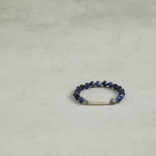 Blue faceted beaded bracelet with a white central bead and silver decorative spacers on gray surface