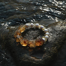 Handcrafted bracelet with amber stones and white pearls on wet rock near water
