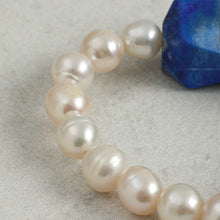 Close-up of a pearl necklace with a large blue gemstone on a grey textured surface
