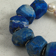 Close-up of faceted blue lapis lazuli gemstone beads and pearls on a grey surface
