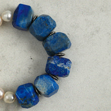 Close-up of blue lapis lazuli beads with small silver spacers and white pearls on gray background