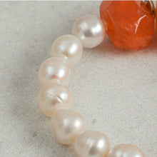 Close-up of white pearls next to a rough orange gemstone on a light gray surface