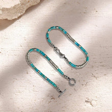Turquoise and silver beaded bracelet with secure clasp on textured stone surface