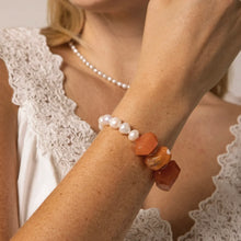 Woman wearing a pearl necklace and a bracelet with white pearls and large orange stones