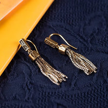 Elegant gold tassel earrings with chain details on dark textured fabric background