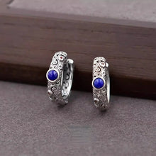 Intricate silver hoop earrings with blue stones and red accents on a wooden surface