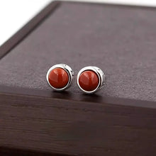 Pair of silver stud earrings with polished round red coral stones on dark wooden surface
