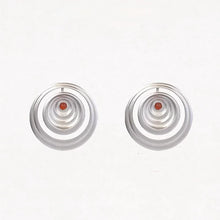 Silver concentric circle earrings with small red gemstone center on white background