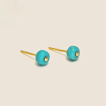 Pair of gold stud earrings with round turquoise stone beads on a light background