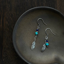 Silver feather earrings with blue and turquoise beads on a dark ceramic plate