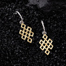 Gold geometric loop dangle earrings with silver hoops on black textured surface
