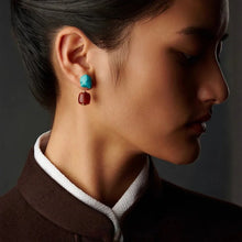 Close-up profile of woman wearing turquoise and red stud earrings with brown collar and white trim