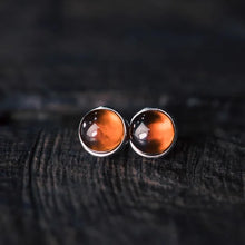 Pair of round amber stud earrings with silver setting on dark textured surface