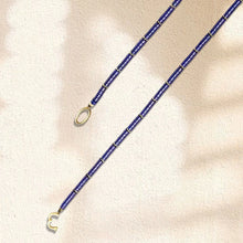 Blue beaded necklace with gold accents and clasp on light textured background