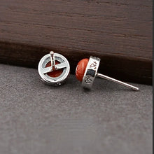 Silver stud earrings with orange round stones and engraved design on metal setting on dark surface