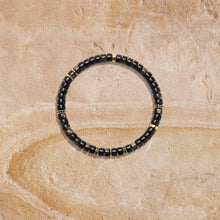Black and gold beaded bracelet laid flat on textured beige stone surface