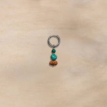 Silver hoop earring with green and turquoise beads and a brown carved pendant on beige background