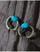 Pair of gold hoop earrings with vibrant blue turquoise stones on textured wood surface