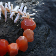 Close-up of orange faceted beads and white coral pieces on dark textured surface