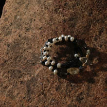 Pearl and black bead bracelet with crystal stones on textured brown rock surface