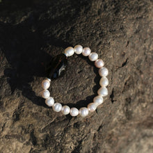 Pearl bracelet with a large black stone bead resting on a textured rock surface in natural light