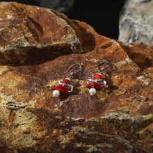 Silver earrings with red coral, clear beads, and white pearls on textured brown rock