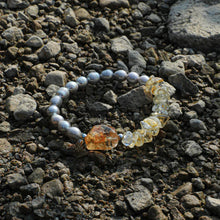 Bracelet with grey pearls and yellow citrine stones on rocky surface