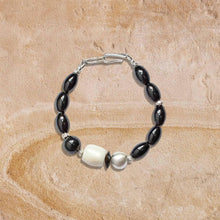Black and white beaded bracelet with silver clasp on textured beige surface