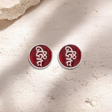 Pair of round red enamel earrings with white abstract design on a textured beige surface