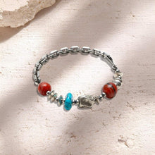 Silver chain bracelet with red, turquoise, and silver bead accents on textured surface