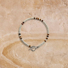 Silver beaded bracelet with brown stone accents and toggle clasp on textured beige surface
