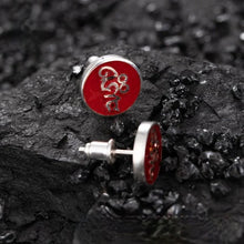 Silver stud earrings with red circular faces and intricate design, placed on black textured surface