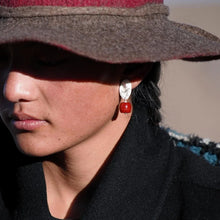 Close-up of a person wearing a brown felt hat, silver and red dangle earrings, and a black coat