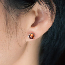 Close-up of ear wearing a small silver stud earring with round polished amber gemstone
