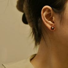 Close-up of ear wearing round brown stud earring with green center on blurred background