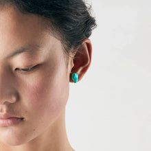 Close-up of a woman wearing a turquoise stud earring on a white background