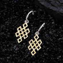 Gold-tone intricate geometric dangle earrings with textured silver hooks on black textured surface