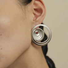 Close-up of ear wearing modern silver circular hoop earring with spiral design and red bead