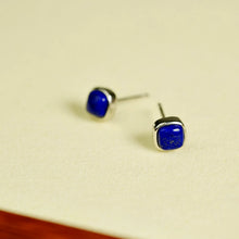 Pair of silver stud earrings with square blue lapis lazuli stones on cream surface