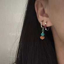 Close-up of ear with layered earrings featuring silver hoops and colorful beads in red, green, and brown