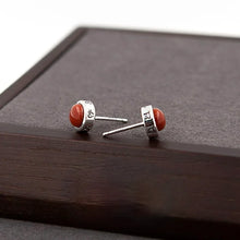 Silver stud earrings with round red stones and engraved details on dark wooden surface