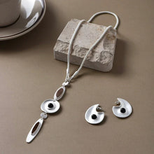 silver necklace with geometric pendant and matching earrings with black stone accents on tan surface