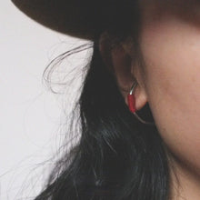 Close-up of a person's ear wearing a red beaded hoop earring with black hair and a beige background